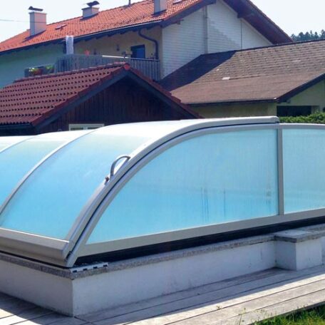 Überdachter Swimmingpool im Garten vor Wohnhäusern, transparente Poolüberdachung schützt vor Witterung. HANSEL.kraus metalltechnik gmbh