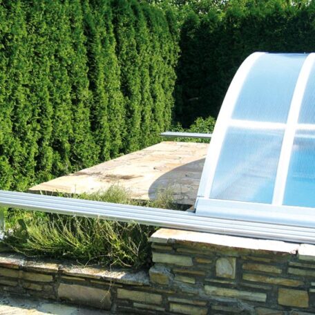 Teilweise abgedeckter Swimmingpool im Garten mit Sichtschutzhecke und gemauerter Steinmauer. HANSEL.kraus metalltechnik gmbh