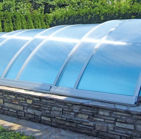 Gewölbte Poolüberdachung mit Glasmodulen auf gemauerter Steinbasis, umgeben von Grün. HANSEL.kraus metalltechnik gmbh