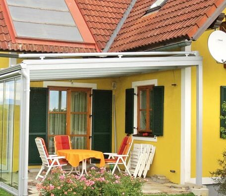 Gelbe Hausfassade mit überdachter Terrasse, Tisch und vier Stühlen, sonniger Gartenszene. HANSEL.kraus metalltechnik gmbh