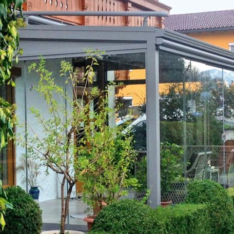 Modernes Glas-Terrassendach mit Pflanzen und Sträuchern, Einfamilienhaus im Hintergrund. HANSEL.kraus metalltechnik gmbh