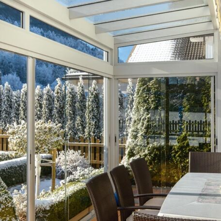 Wintergarten mit Glasterrasse, Essbereich und Blick auf verschneiten Garten und Tannen. HANSEL.kraus metalltechnik gmbh