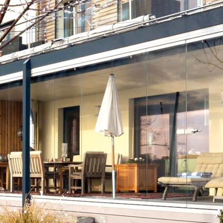 Terrasse mit Glasüberdachung, Gartentisch, Stühlen und Sonnenschirm vor modernem Wohnhaus. HANSEL.kraus metalltechnik gmbh