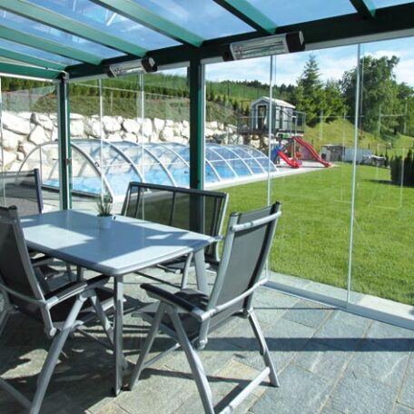 Überdachte Terrasse mit Sitzgruppe, Blick auf Garten, Spielplatz und überdachtem Pool. HANSEL.kraus metalltechnik gmbh