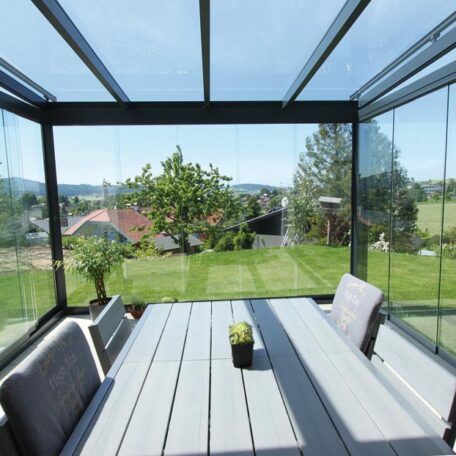 Terrasse mit verglastem Wintergarten, Esstisch und Blick auf grünen Garten im Sommer. HANSEL.kraus metalltechnik gmbh