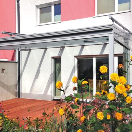 Moderne Terrassenüberdachung mit Glas und gelben Rosen vor einem Einfamilienhaus. HANSEL.kraus metalltechnik gmbh