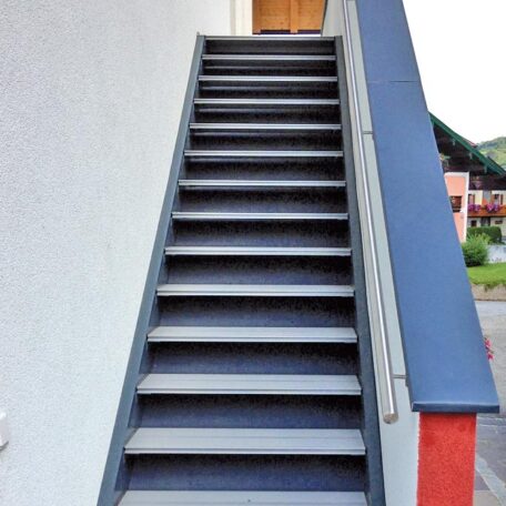 Außentreppe mit Geländer führt zu einer Holztür, Hauswand links, Tageslicht. HANSEL.kraus metalltechnik gmbh