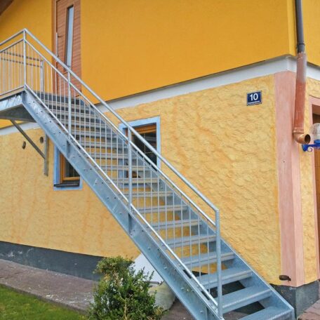 Außentreppe aus Metall führt an gelber Hausfassade zu einer erhöhten Haustür. HANSEL.kraus metalltechnik gmbh