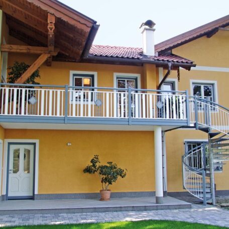 Gelbes Einfamilienhaus mit Balkon, moderner Außentreppe und kleinem Baum im Eingangsbereich. de HANSEL.kraus metalltechnik gmbh