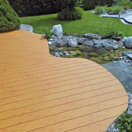Holzterrasse mit geschwungener Kante an einem Teich, umgeben von Rasen und Steinen. de HANSEL.kraus metalltechnik gmbh