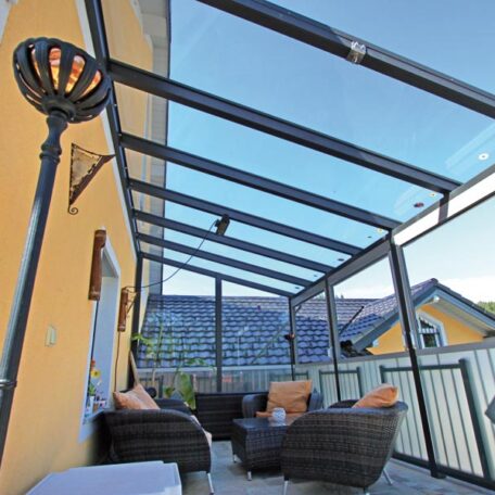 Gemütlicher Balkon mit Glasdach, Sitzgruppe und Blick auf Nachbarhäuser bei Sonnenschein. de HANSEL.kraus metalltechnik gmbh