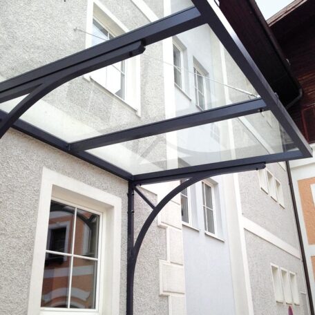 Modernes Vordach aus Glas und Stahl an einem Mehrfamilienhaus, seitliche Fenster sichtbar. HANSEL.kraus metalltechnik gmbh