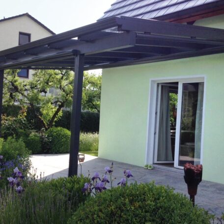 Terrassenüberdachung aus Metall an modernem, hellgrünem Haus mit Gartenzugang und Blumen. de HANSEL.kraus metalltechnik gmbh
