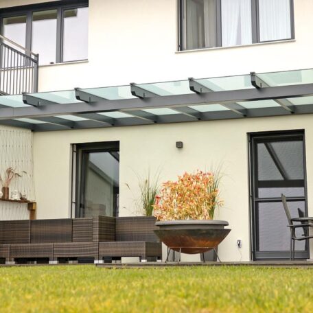 Moderne Terrasse mit Glasüberdachung, Sitzmöbeln und Feuerstelle vor einem Einfamilienhaus. HANSEL.kraus metalltechnik gmbh