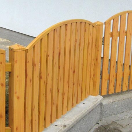 Holzzaun mit gebogenem Abschluss steht auf grauer Betoneinfassung vor einer weißen Wand. HANSEL.kraus metalltechnik gmbh