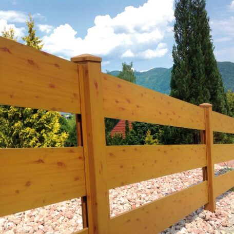 Moderner Holzzaun vor Gartenlandschaft mit Bäumen, Kiesweg und Bergen im Hintergrund. HANSEL.kraus metalltechnik gmbh