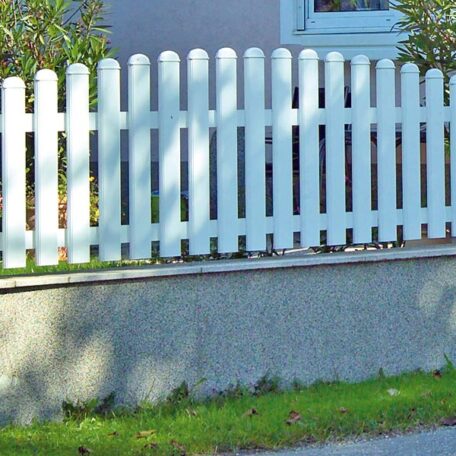 Weißer Gartenzaun vor einem Haus mit Rasen und kleinen Büschen, Fenster im Hintergrund. HANSEL.kraus metalltechnik gmbh