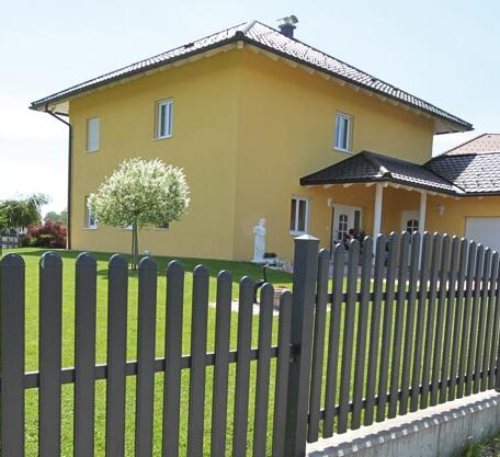 Ein gelbes Einfamilienhaus mit Garten, Baum und modernem Metallzaun im Vordergrund. HANSEL.kraus metalltechnik gmbh