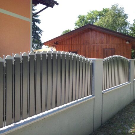 Moderner Metallzaun vor einem orangefarbenen Wohnhaus, im Hintergrund steht ein Holzhaus. de HANSEL.kraus metalltechnik gmbh