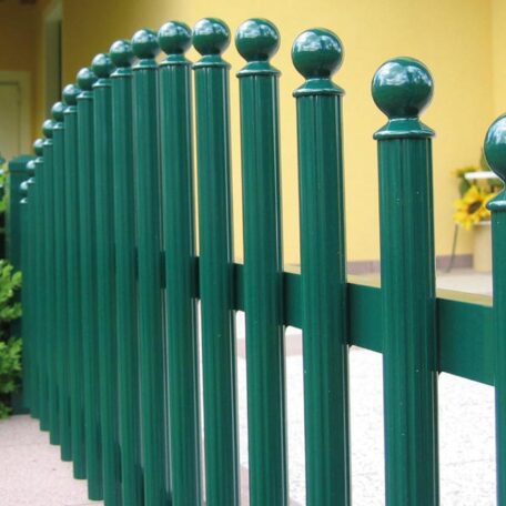 Grüner Metallzaun mit runden Pfosten vor gelber Hauswand, moderner Gartenzaun. HANSEL.kraus metalltechnik gmbh
