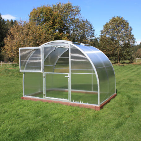Kleines Gewächshaus aus Glas steht auf einer grünen Wiese vor Bäumen im Freien. HANSEL.kraus metalltechnik gmbh