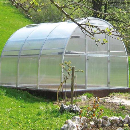 Gewächshaus aus Kunststoff steht auf grüner Wiese neben Hang im Frühling. HANSEL.kraus metalltechnik gmbh