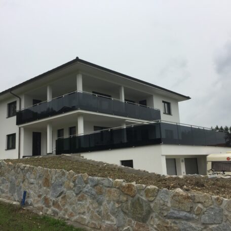 Modernes zweistöckiges Wohnhaus mit dunklen Balkongeländern und Steinsockel, Hanglage. HANSEL.kraus metalltechnik gmbh