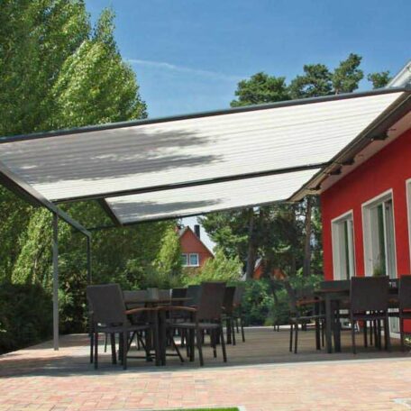 Sonnensegel spendet Schatten über Sitzgruppe im Garten neben rotem Haus bei Sonnenschein. HANSEL.kraus metalltechnik gmbh