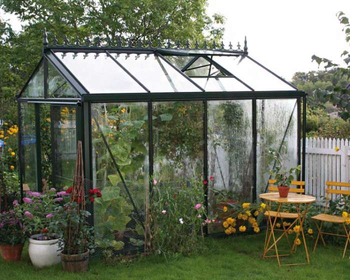 Glashaus im Garten mit Pflanzen und kleinem gelben Tisch mit zwei Stühlen davor. HANSEL.kraus metalltechnik gmbh