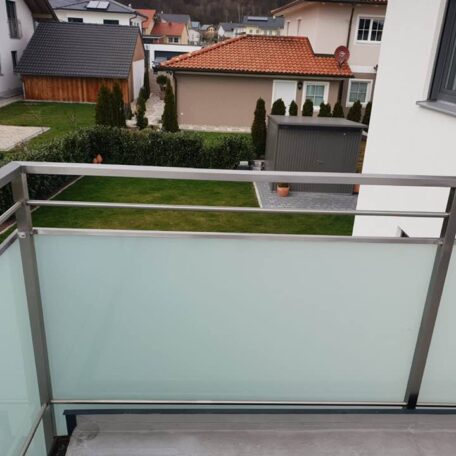 Blick von einem Balkon mit Milchglasgeländer auf gepflegten Garten und Nachbarhäuser. HANSEL.kraus metalltechnik gmbh