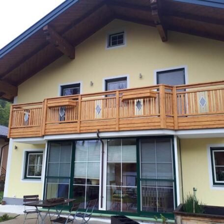 Gelbes Haus mit Holz-Balkon und großen Fenstern, Ansicht von außen. de HANSEL.kraus metalltechnik gmbh