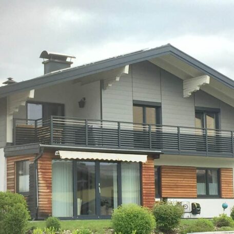 Modernes Einfamilienhaus mit Balkon, großen Fenstern und Garten unter bewölktem Himmel. HANSEL.kraus metalltechnik gmbh