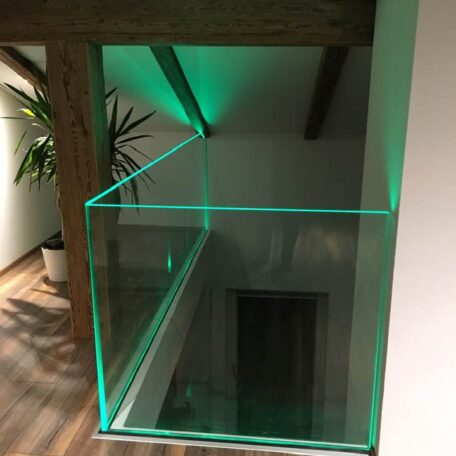 Modernes Glasgeländer mit grüner Beleuchtung im Flur eines Dachgeschosses, Holzbalken sichtbar. HANSEL.kraus metalltechnik gmbh