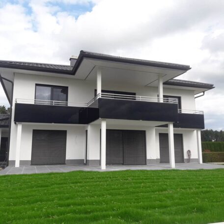 Modernes zweistöckiges Einfamilienhaus mit Balkon, weißen Wänden und großem Garten unter bewölktem Himmel. HANSEL.kraus metalltechnik gmbh