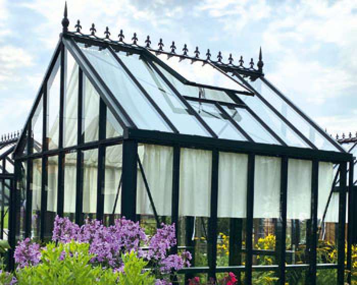 Gewächshaus mit Glasdach und schwarzen Rahmen, davor blühende Blumen im Garten. HANSEL.kraus metalltechnik gmbh