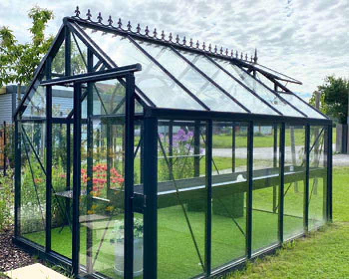 Glashaus mit schwarzem Metallrahmen steht auf Rasenfläche, innen Pflanzen, im Hintergrund Bäume. HANSEL.kraus metalltechnik gmbh