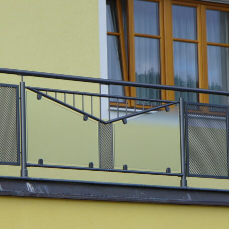 Metallgeländer mit modernem Muster vor gelber Fassade und großem Fenster, Balkonansicht. HANSEL.kraus metalltechnik gmbh