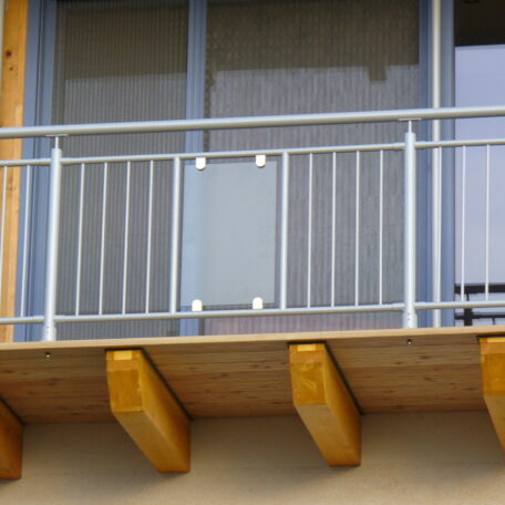 Moderner Balkon mit Metallgeländer und Holzträgern an einer Hausfassade, Detailaufnahme. HANSEL.kraus metalltechnik gmbh