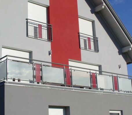 Modernes Wohnhaus mit rotem Fassadenstreifen und Glasbalkonen, Sonnenschutz an den Fenstern. HANSEL.kraus metalltechnik gmbh