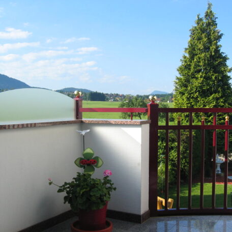 Blick von Balkon auf grüne Wiese, Baum, Berge und blauen Himmel im Hintergrund. HANSEL.kraus metalltechnik gmbh