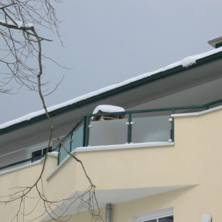 Ein schneebedeckter Balkon an einem modernen, gelben Wohngebäude unter grauem Himmel. HANSEL.kraus metalltechnik gmbh