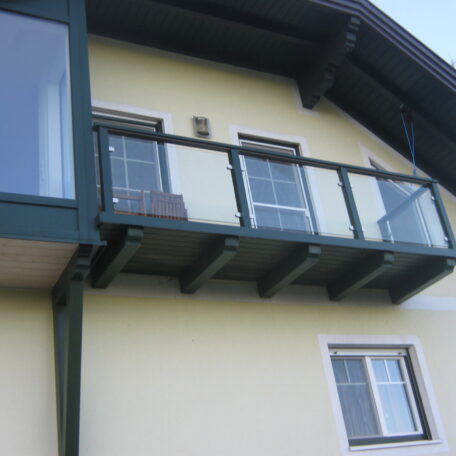 Balkon mit Glasgeländer an gelbem Haus, darunter Fenster, moderner Stil. HANSEL.kraus metalltechnik gmbh