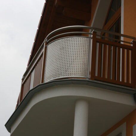 Moderner Balkon mit kombinierter Holz- und Metallbrüstung an einem orangefarbenen Haus, Tageslicht. HANSEL.kraus metalltechnik gmbh