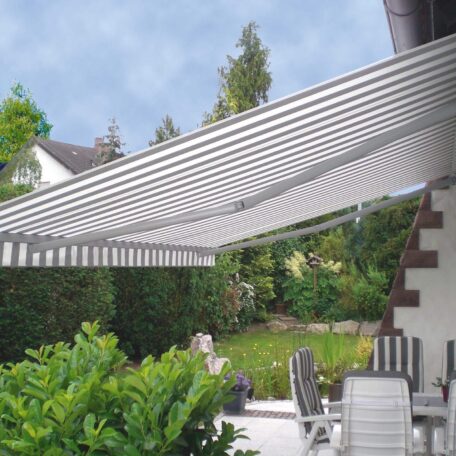 Gestreifte Markise spendet Schatten auf gemütlicher Terrasse mit Garten und Sitzmöbeln. HANSEL.kraus metalltechnik gmbh