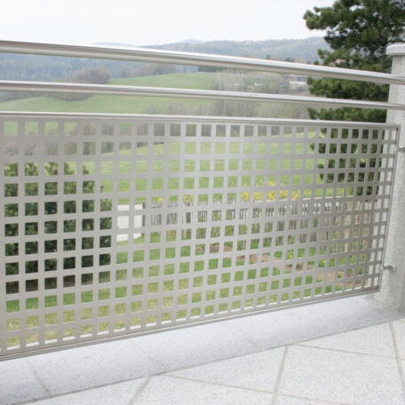 Geländer aus Edelstahl mit quadratischem Lochmuster auf einer Terrasse, Landschaft im Hintergrund. HANSEL.kraus metalltechnik gmbh