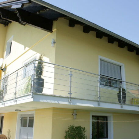 Gelbes modernes Einfamilienhaus mit Balkon und Edelstahlgeländer, sonniger Himmel im Hintergrund. HANSEL.kraus metalltechnik gmbh
