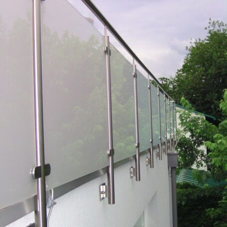 Modernes Balkongeländer aus Milchglas und Edelstahl vor grünem Garten und Himmel. HANSEL.kraus metalltechnik gmbh