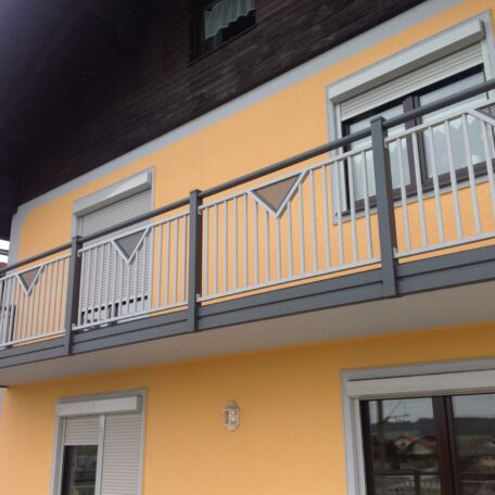 Balkon mit modernem Metallgeländer an gelber Hausfassade, Fenster mit Rollläden, Tageslicht. HANSEL.kraus metalltechnik gmbh