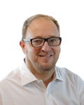 Porträt eines lächelnden Mannes mit Brille und weißem Hemd vor weißem Hintergrund. HANSEL.kraus metalltechnik gmbh