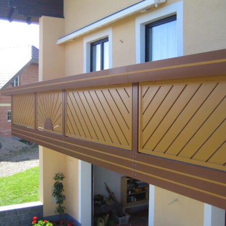 Moderner Holzbalkon mit gelben und braunen Paneelen an einem Einfamilienhaus bei Tageslicht. HANSEL.kraus metalltechnik gmbh